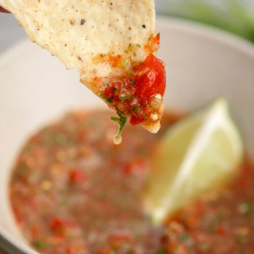 Tortilla chip being dipped into a garden fresh salsa with a wedge of lime in the background